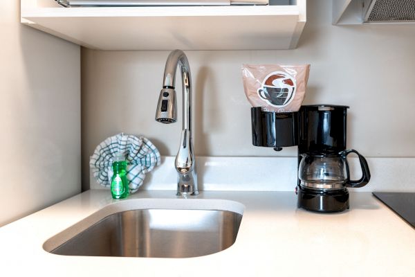 A kitchen sink with a faucet, a coffee maker with a cup holder, a cleaning cloth, and a dish soap bottle on the counter.