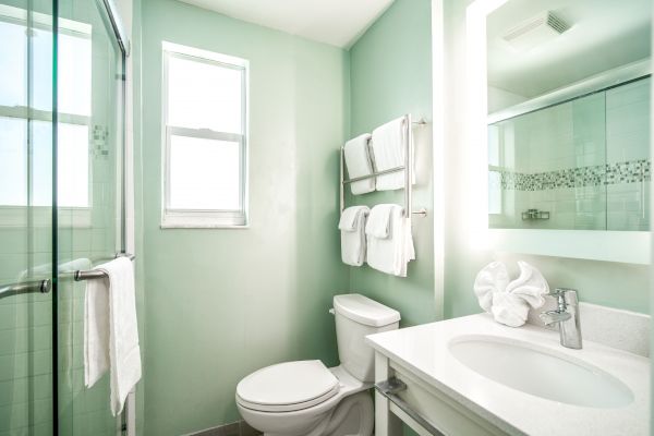 A small, modern bathroom with light green walls, a shower, a toilet, a sink with a mirror, and neatly arranged towels.