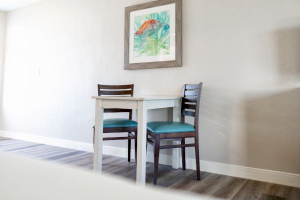 Two chairs with blue cushions are placed next to a small table. A framed artwork hangs above them on the wall.