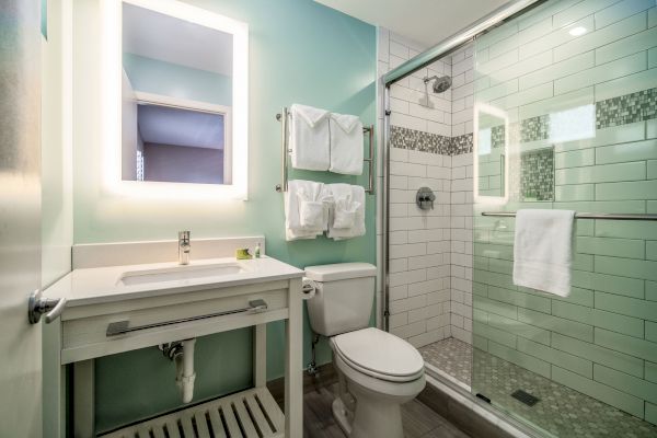 A modern bathroom with a shower, toilet, and vanity. It has white tiles, a glass shower door, and neatly folded towels on racks.