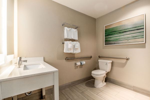 This image shows a clean, minimalistic bathroom with a sink, toilet, towel rack, and a green-themed artwork on the wall, complete.