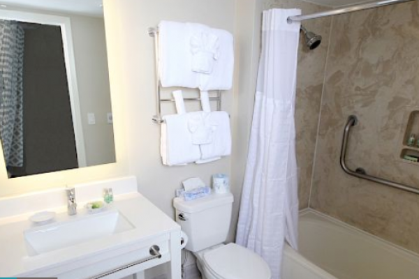 A bathroom with a sink, mirror, toilet, towels on a rack, and a bathtub with a shower curtain and grab bar.