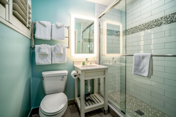 A modern bathroom with a toilet, sink, mirror, and a glass shower stall. Towels are neatly hung above the toilet and on the shower door.